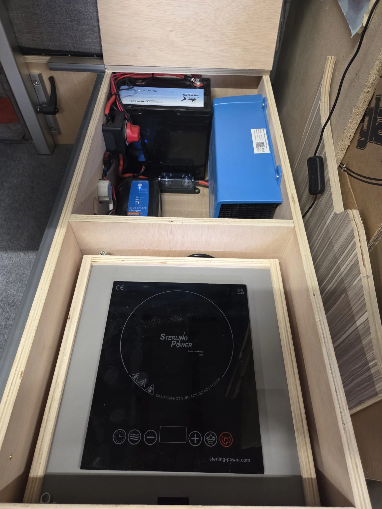 Dream Catcher Power Up Bundle battery, inverter and induction hob installed inside an open Camper Pod storage compartment.